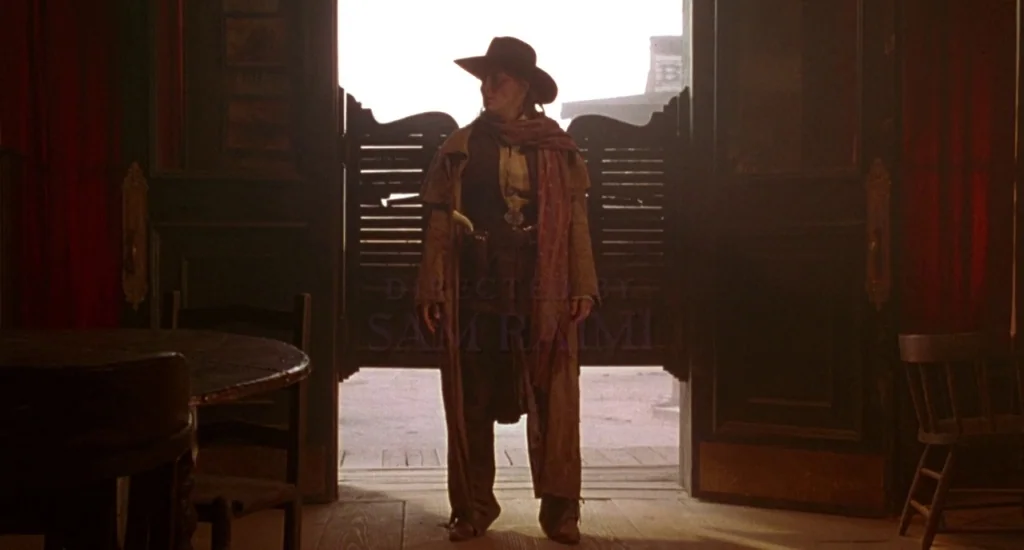 The Quick and the Dead (1995) movie still: fullbody — A dimly lit western saloon has an open entryway leading to a bright street. A woman in a…