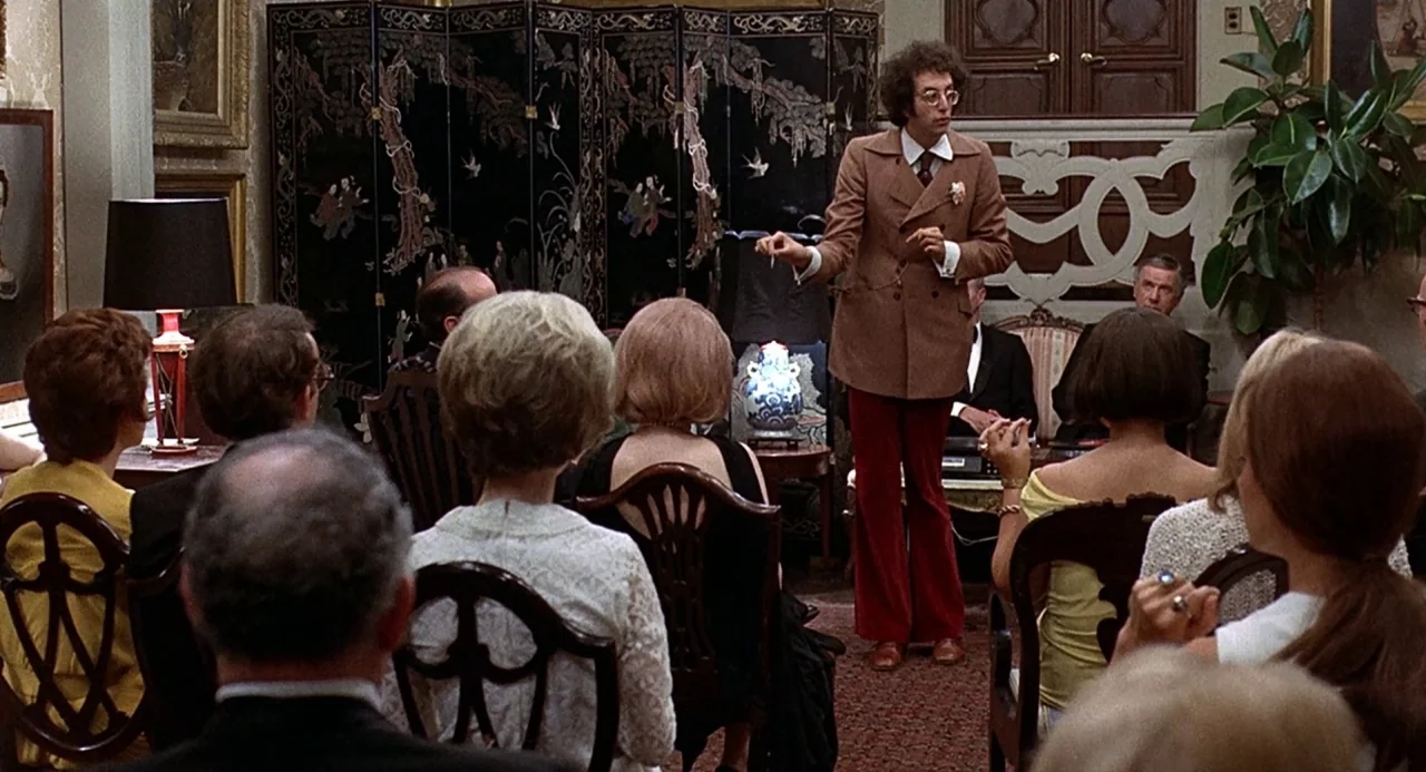 Taking Off (1971) movie still: medium — A crowded parlor with ornate chairs and an Asian-style folding screen in the back. A man stands in the…