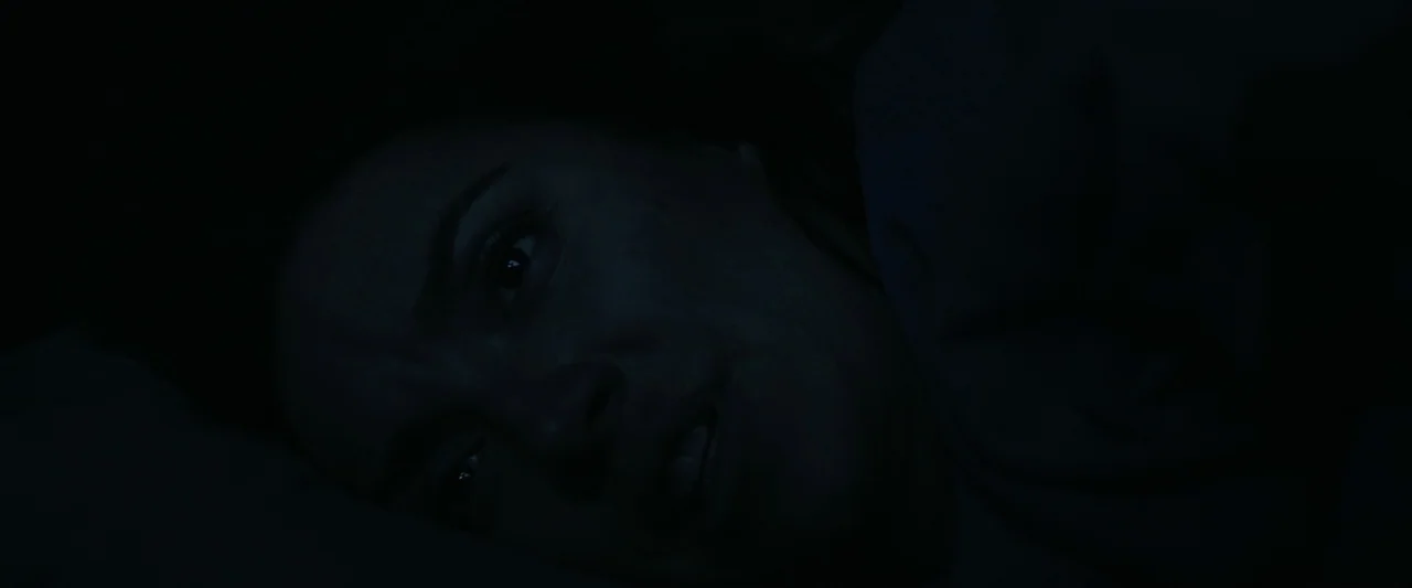 Sign Here (2017) movie still: closeup — A dark bedroom interior with the subject lying in bed at night. A woman lies partially visible in shadow…