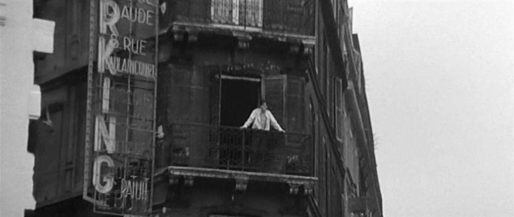 Antoine and Colette (1962) movie still: wide — An old Parisian apartment building features a prominent vertical metal sign on the corner. A man…