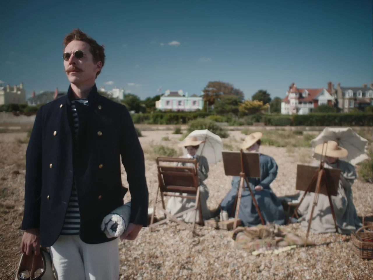 The Electrical Life of Louis Wain (2021) movie still: medium — A pebble beach setting features a man in the foreground and three painters beyond.…