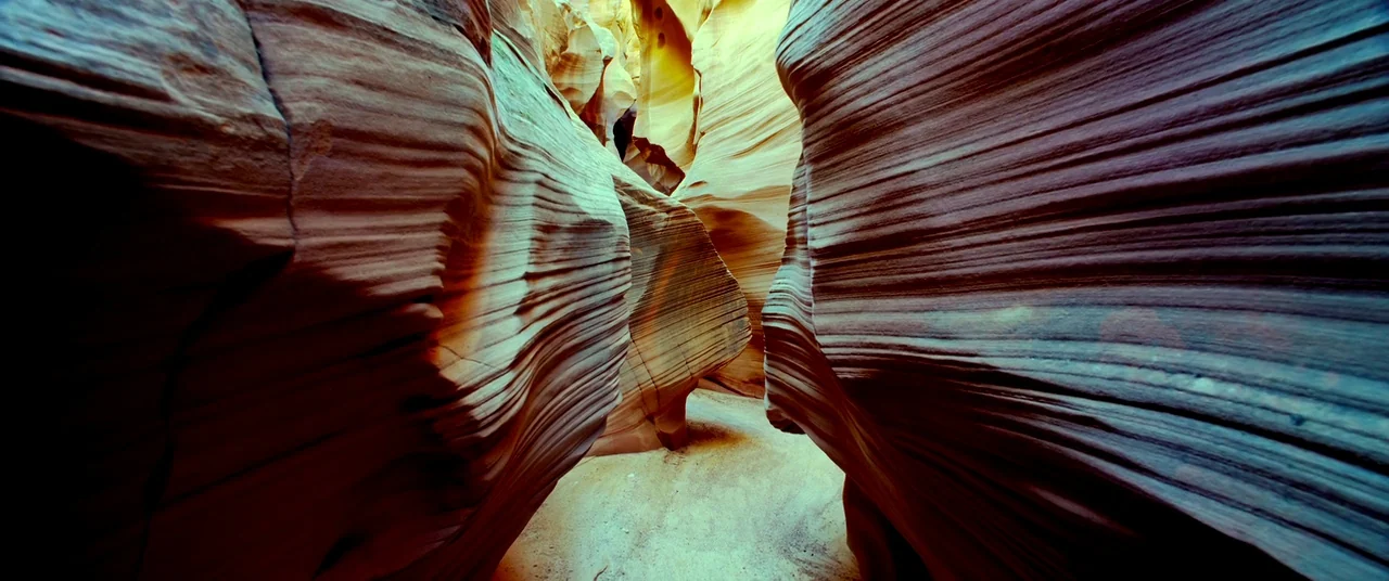 Samsara (2011) movie still: establishing — A narrow slot canyon features curved, wind-swept walls of layered red and orange sandstone. The rocky…
