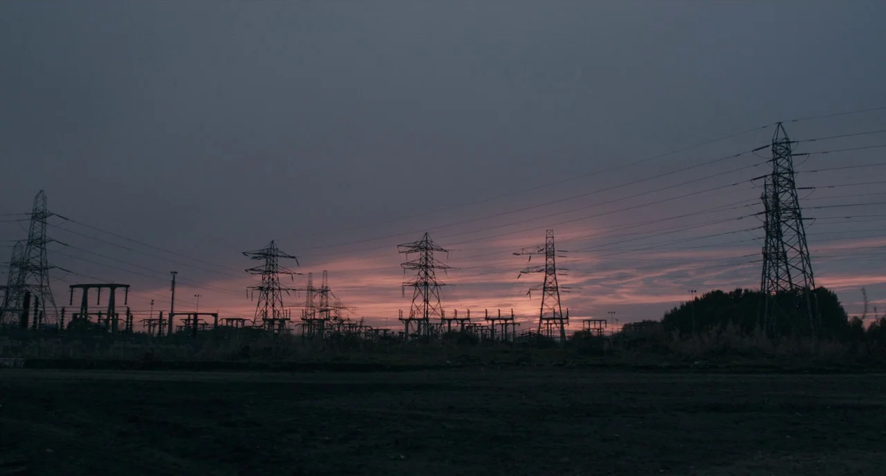 The Selfish Giant (2013) movie still: establishing — A field of metal electrical transmission towers stands against a muted, pink-tinted dusk sky.…