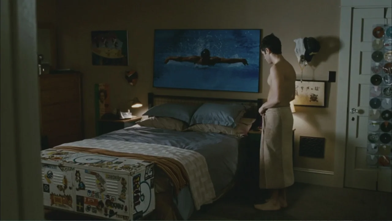 The Stepfather (2009) movie still: fullbody — A modest bedroom contains a bed with a large framed swimming photo above it. A young man stands beside…