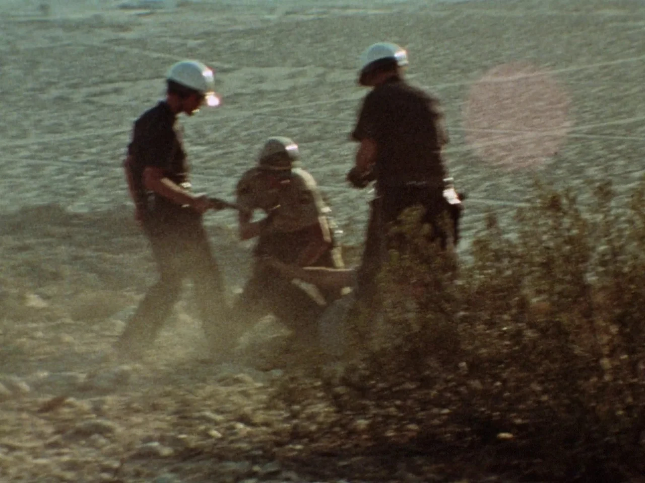 Punishment Park (1971) movie still: fullbody — A rocky, dry desert landscape stretches out under bright, direct sunlight. Three uniformed officers…