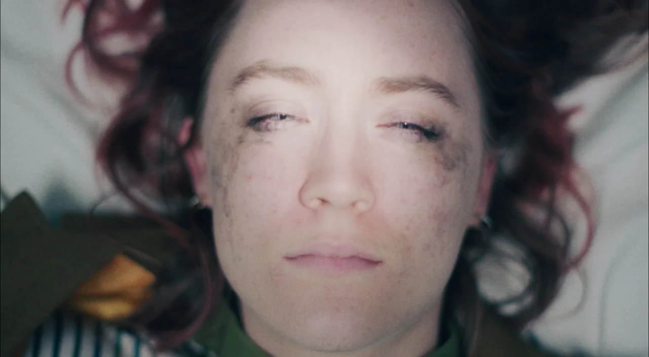 Lady Bird (2017) movie still: closeup — A woman lies on a white surface with messy hair and dark smudges. She is positioned frontally with her eyes…