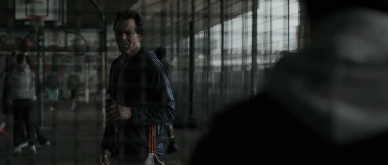 Doctor Strange (2016) movie still: medium — An enclosed outdoor basketball court with chain-link fencing serves as the background. A middle-aged man…