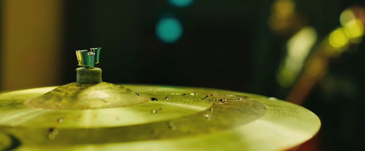 Whiplash (2014) movie still: closeup — A close-up of a bronze-colored drum cymbal featuring scattered water droplets on its surface. The background…