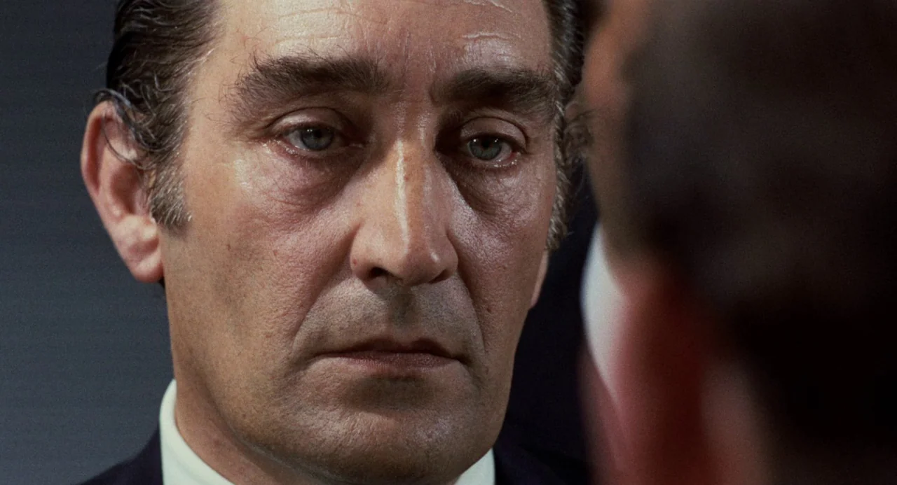 Investigation of a Citizen Above Suspicion (1970) movie still: closeup — A man in a suit looks directly forward in an interior setting. He stands…