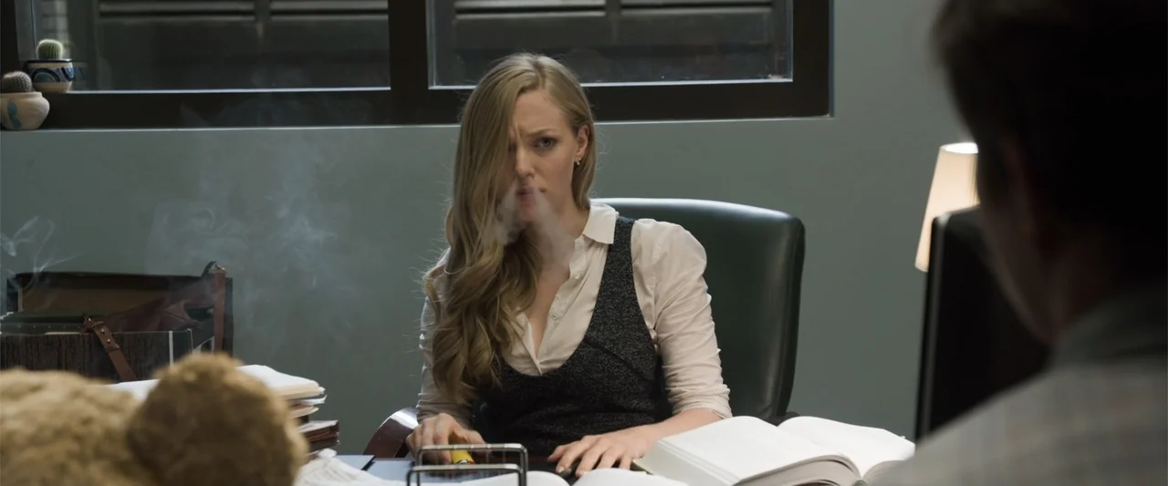 Ted 2 (2015) movie still: medium — A modern professional office with grey walls and a large window in background. A blonde woman in a vest exhales…
