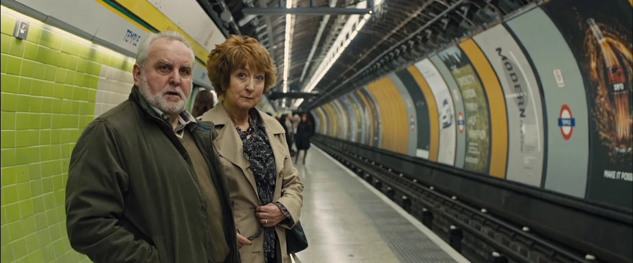 Skyfall (2012) movie still: medium — A London Underground platform with distinctive green tiles and yellow arched advertisement boards. An older…