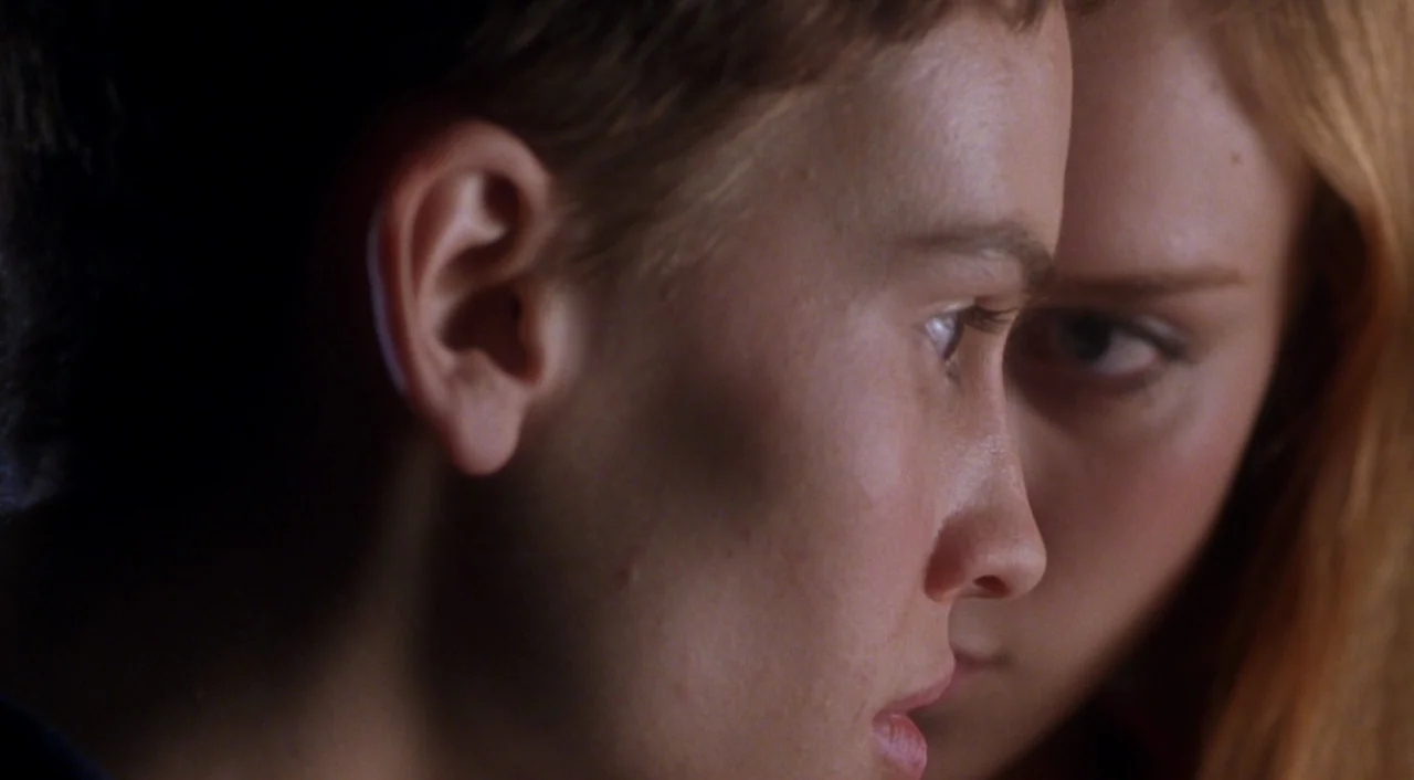 Boys Don’t Cry (1999) movie still: closeup — A close-up shot focuses on the overlapping profiles of two young women indoors. One person is…