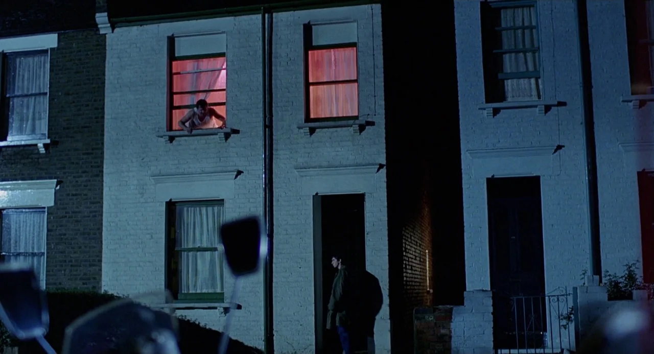 Quadrophenia (1979) movie still: wide — A two-story white brick row house is illuminated by cold moonlight at night. One man looks out from a…