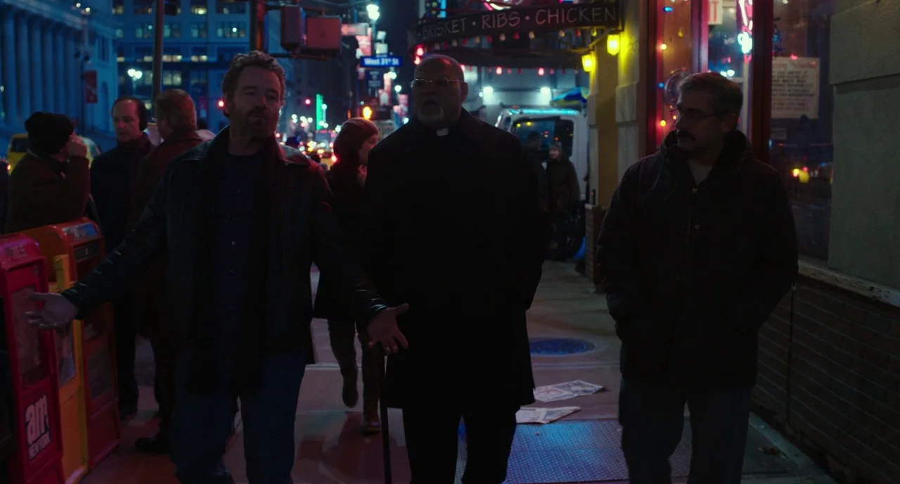 Last Flag Flying (2017) movie still: fullbody — A nighttime city sidewalk passes by a storefront lit with red and yellow neon. Three men stand…