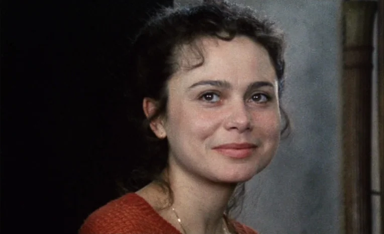 After The Rehearsal (1984) movie still: closeup — A woman stands in a softly lit interior space with a dark background. She faces three-quarters…