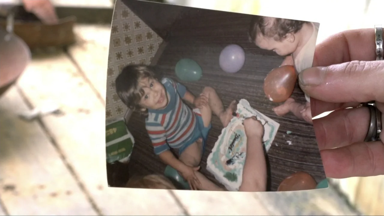 Meth Storm (2017) movie still: closeup — A close-up view shows a hand holding a vintage physical birthday photograph. The photograph depicts a young…
