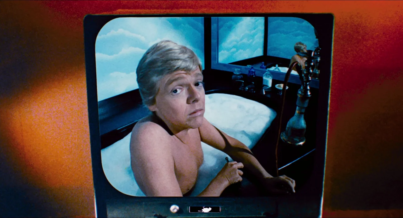 Phantom of the Paradise (1974) movie still: medium — A man sits in a bathtub in front of a blue cloud-painted backdrop. A glass pipe sits on the tub…