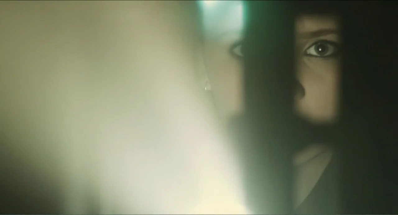 Haunter (2013) movie still: closeup — A dark, cramped interior space is punctuated by a single intense light source flare. A young woman with dark…