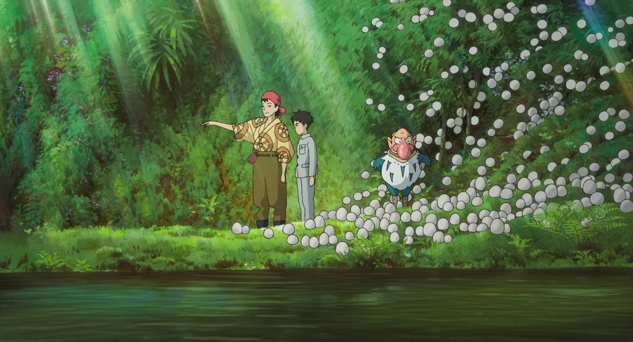 The Boy and The Heron (2023) movie still: wide — A vibrant green riverbank is covered in numerous smooth white stones or eggs. A woman, a boy, and a…