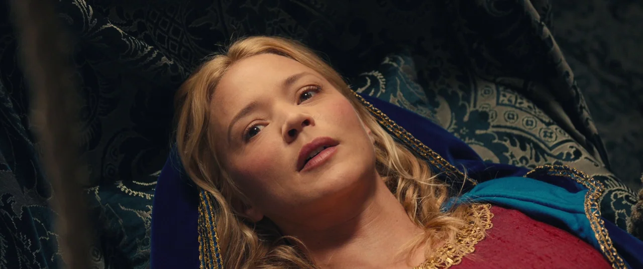 Benedetta (2021) movie still: closeup — A woman lies on a patterned fabric surface inside a draped tent enclosure. She looks upward while wearing…
