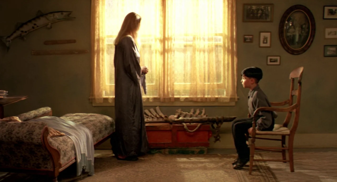 The Reflecting Skin (1990) movie still: fullbody — An interior space features muted green walls decorated with various small framed pictures and…