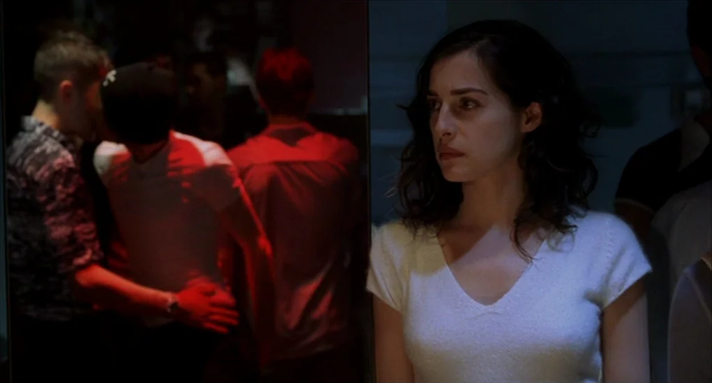 Anatomy of Hell (2004) movie still: medium — A dimly lit nightclub interior with a distinct separation between dance floor and periphery. A woman…
