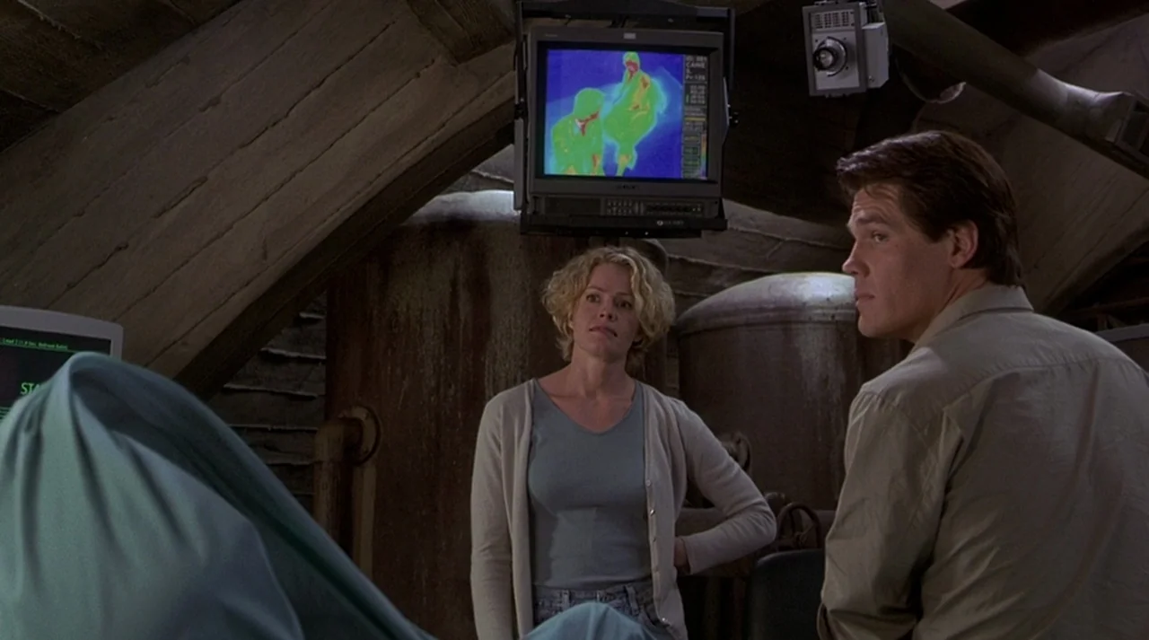 Hollow Man (2000) movie still: medium — A cluttered technical workspace featuring exposed wooden beams and large metal vats in background. A man and…