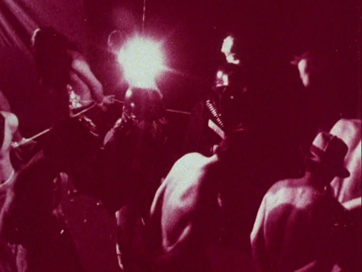 Emperor Tomato Ketchup movie still: medium — A dark, crowded indoor space features several people in silhouette under harsh light. Bare-chested…