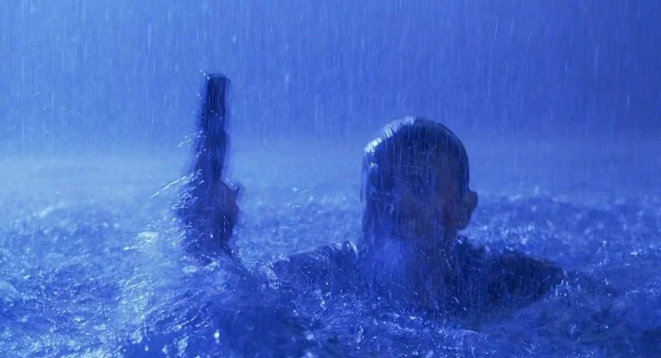 Jurassic Park III (2001) movie still: medium — A person is submerged in water during heavy rain at night. The individual holds a firearm vertically…