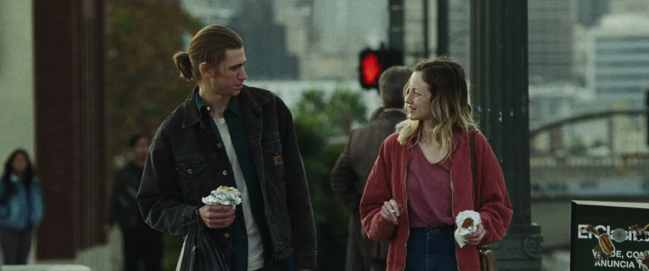 To Leslie (2022) movie still: medium — An urban city street setting with a blurred background showing traffic infrastructure and structures. A man…
