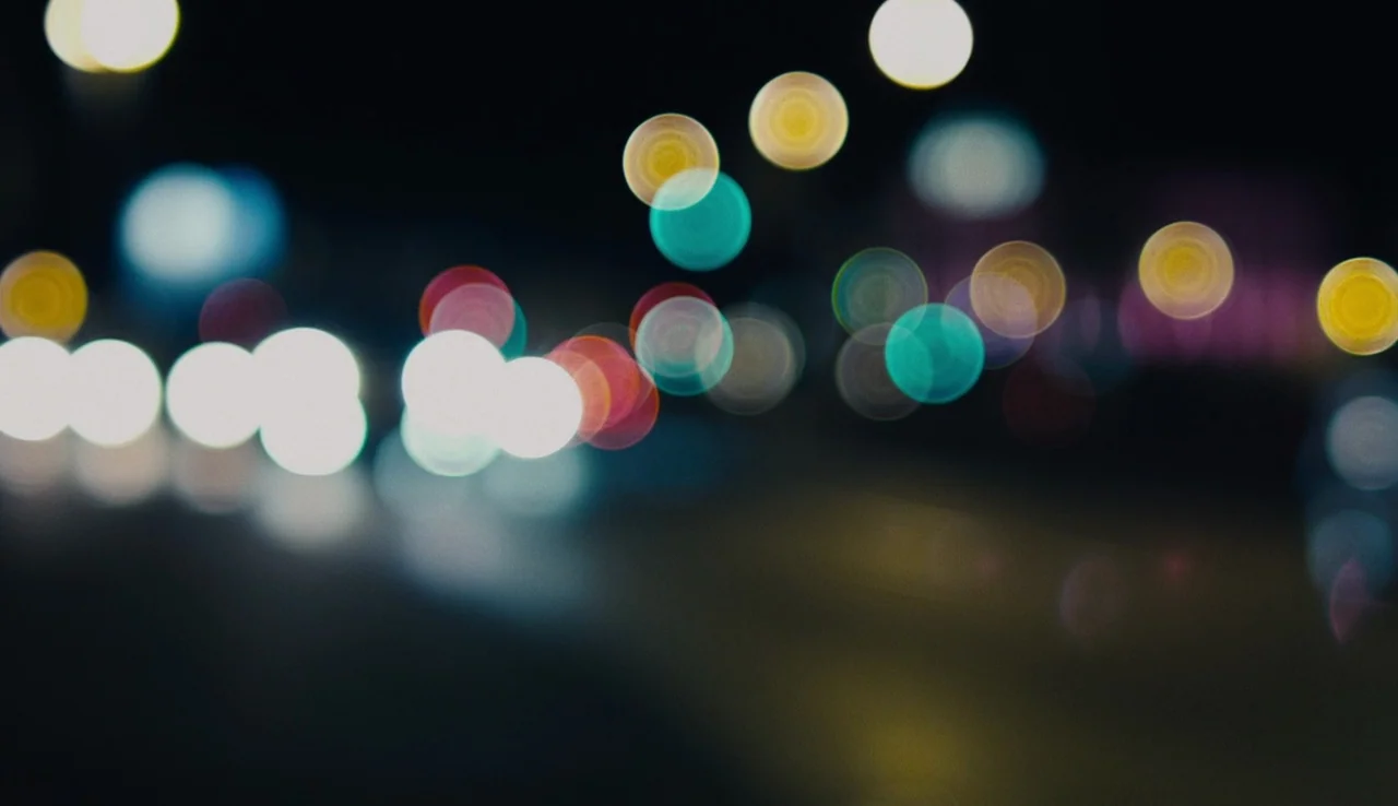 Land Ho! (2014) movie still: establishing — An extremely out-of-focus view of urban night lights against a pitch-black background. Circular light…