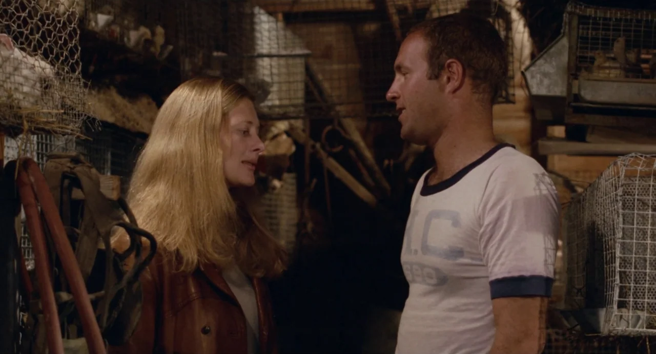 The Rain People (1969) movie still: medium — A dimly lit barn interior filled with metal wire cages and farm equipment. A man and a woman stand…