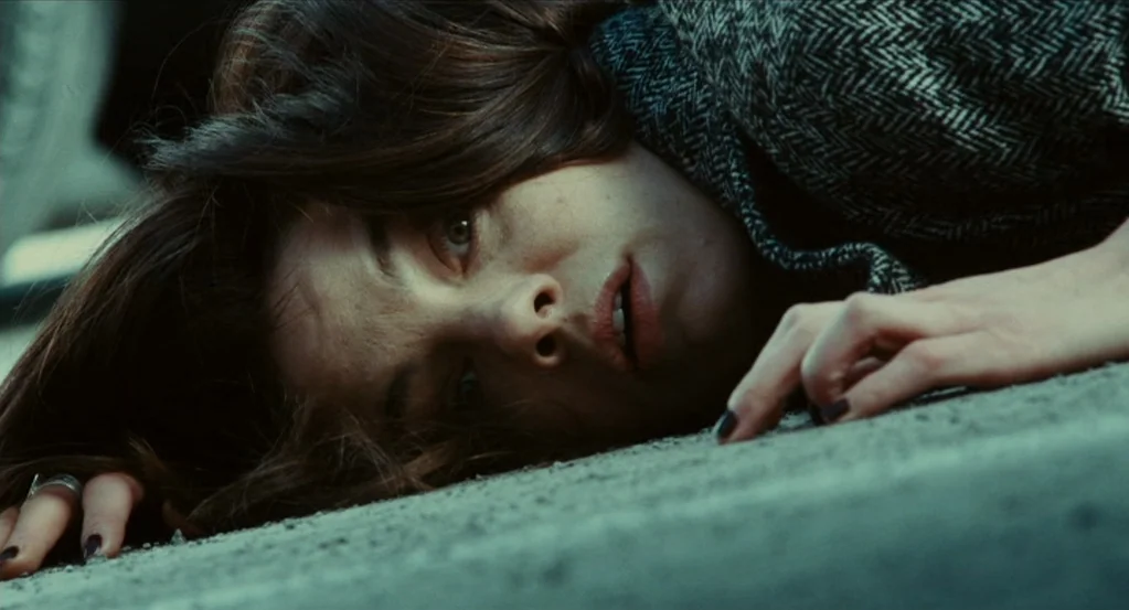 Source Code (2011) movie still: closeup — A woman lies flat against a grey concrete surface. She looks forward with her hair splayed out on the…