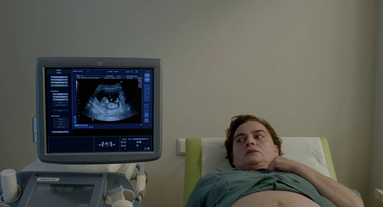 Blackbird Blackbird Blackberry (2023) movie still: medium — A clinical ultrasound room with plain beige walls and a medical examination table. A…
