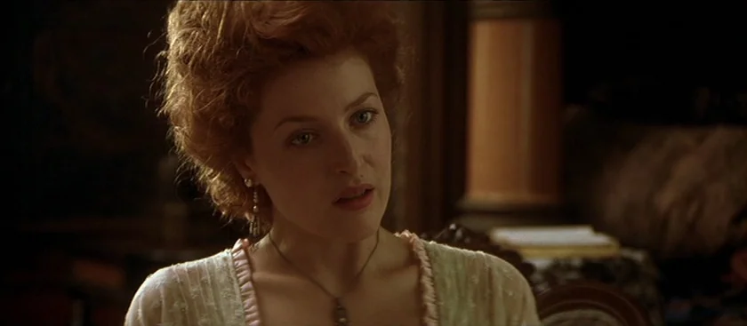 The House of Mirth (2000) movie still: closeup — A dimly lit room features a woman with elaborate hair sitting against dark furniture. She looks…
