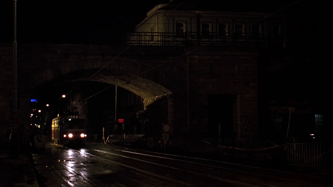 Blade II (2002) movie still: wide — A stone underpass spans over tram tracks in a dark, wet urban setting at night. A brightly lit tram approaches…