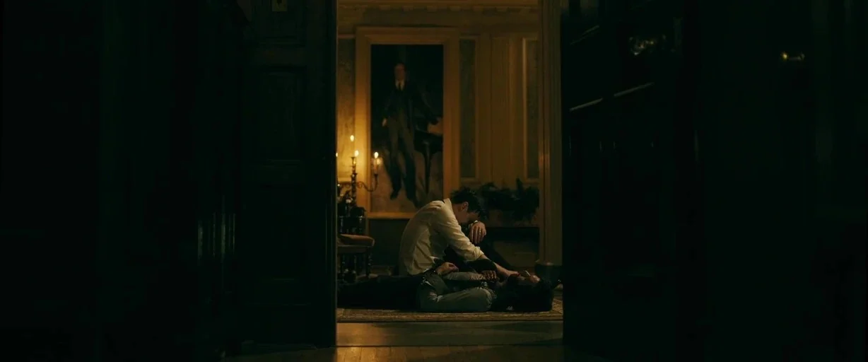 Ready or Not (2019) movie still: wide — A dimly lit grand hallway features a tall portrait hanging between doorway openings. A man in a white shirt…