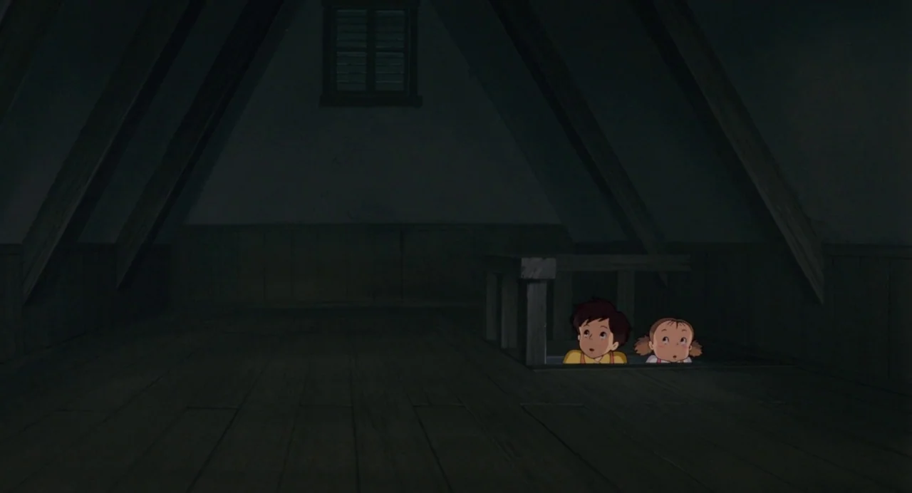 My Neighbour Totoro (1988) movie still: wide — A dark wooden attic with sloping walls and a small central window. Two children watch from an opening…