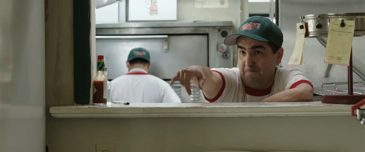 Overboard (2018) movie still: medium — The interior of a working pizza shop counter with kitchen equipment visible in the background. A man wearing…