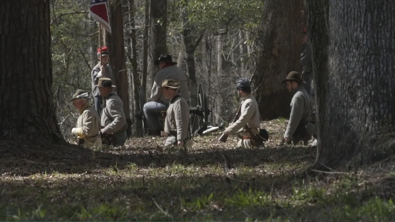 Kill Cavalry (2021) movie still: wide — A group of soldiers in 19th-century military uniforms gather within a dense wooded area. Several men in tan…