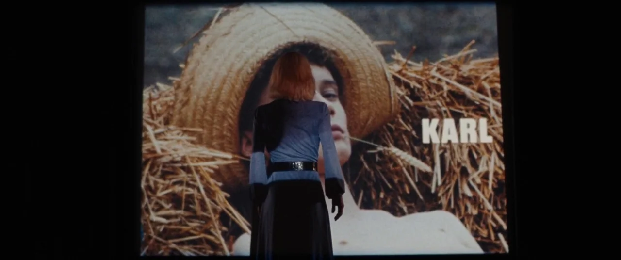 Knife+Heart (2018) movie still: fullbody — A woman stands in a dark theater viewing a large screen. The projected image shows a person in a straw…