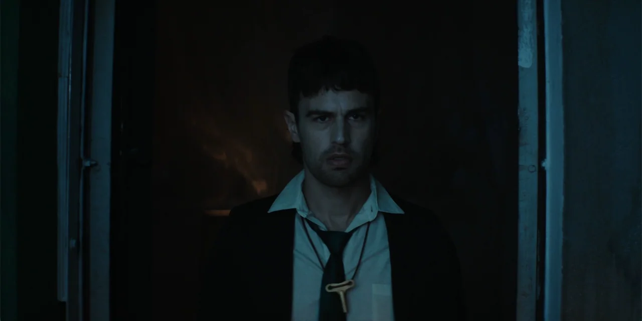The Monkey (2025) movie still: medium — A man stands in a dark doorway against a black background. He is wearing a dress shirt and blazer with a key…