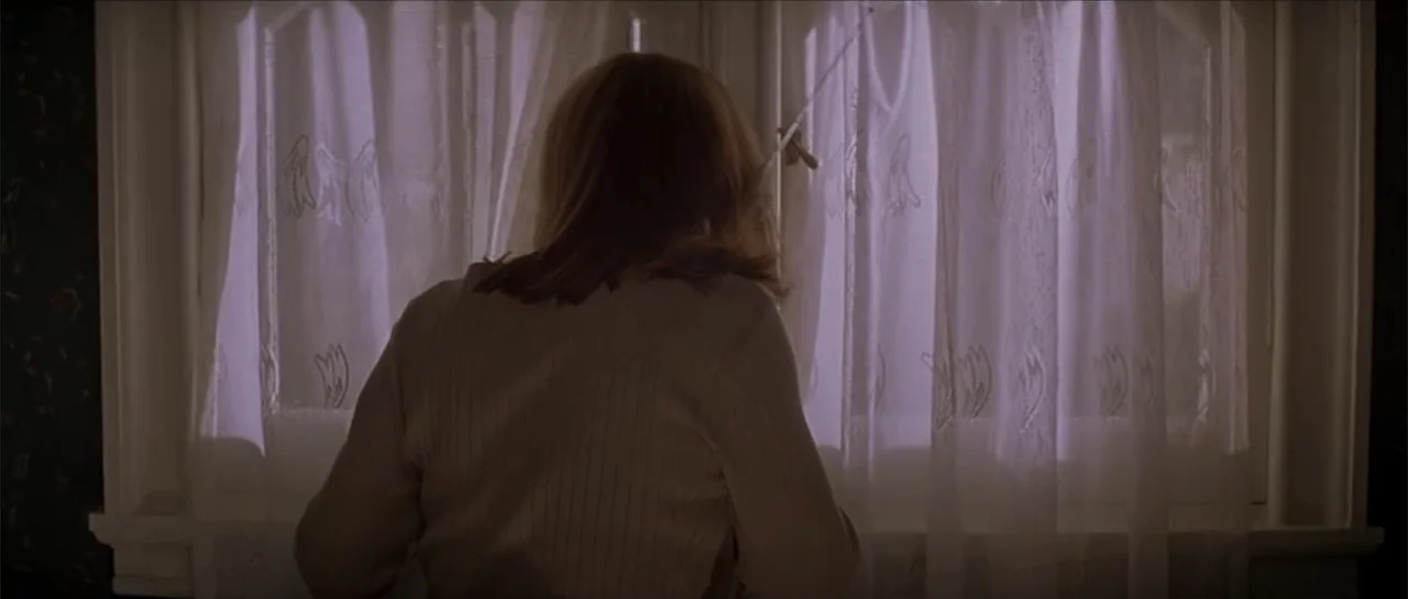 Moonlight and Valentino (1995) movie still: medium — A woman stands in a dark room facing a closed window with white curtains. She observes the…