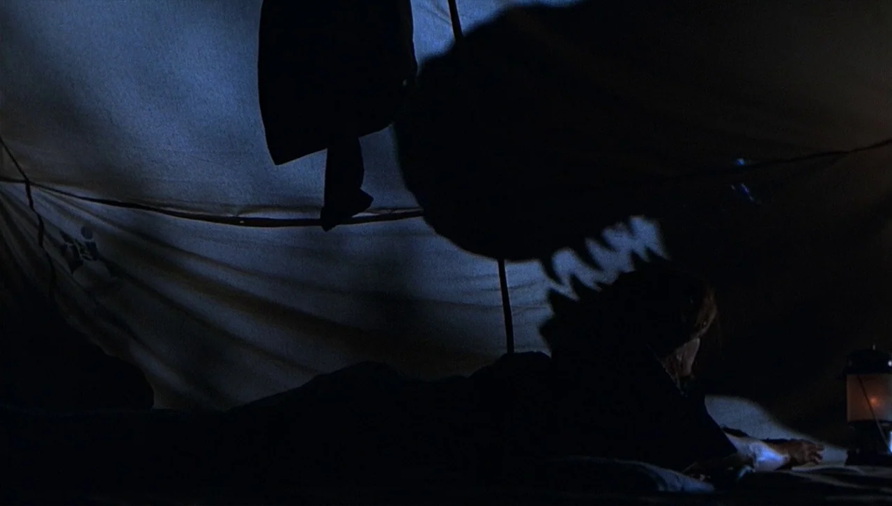 The Lost World: Jurassic Park (1997) movie still: medium — Inside a dark fabric enclosure, a person lies horizontally on the ground. A large,…