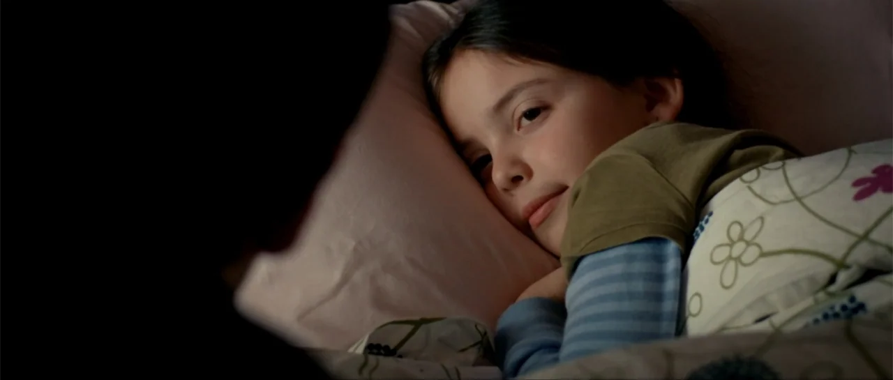 The Rebound (2009) movie still: closeup — A bedroom contains a child resting in a bed with a patterned comforter. The child lies on a pink pillow…