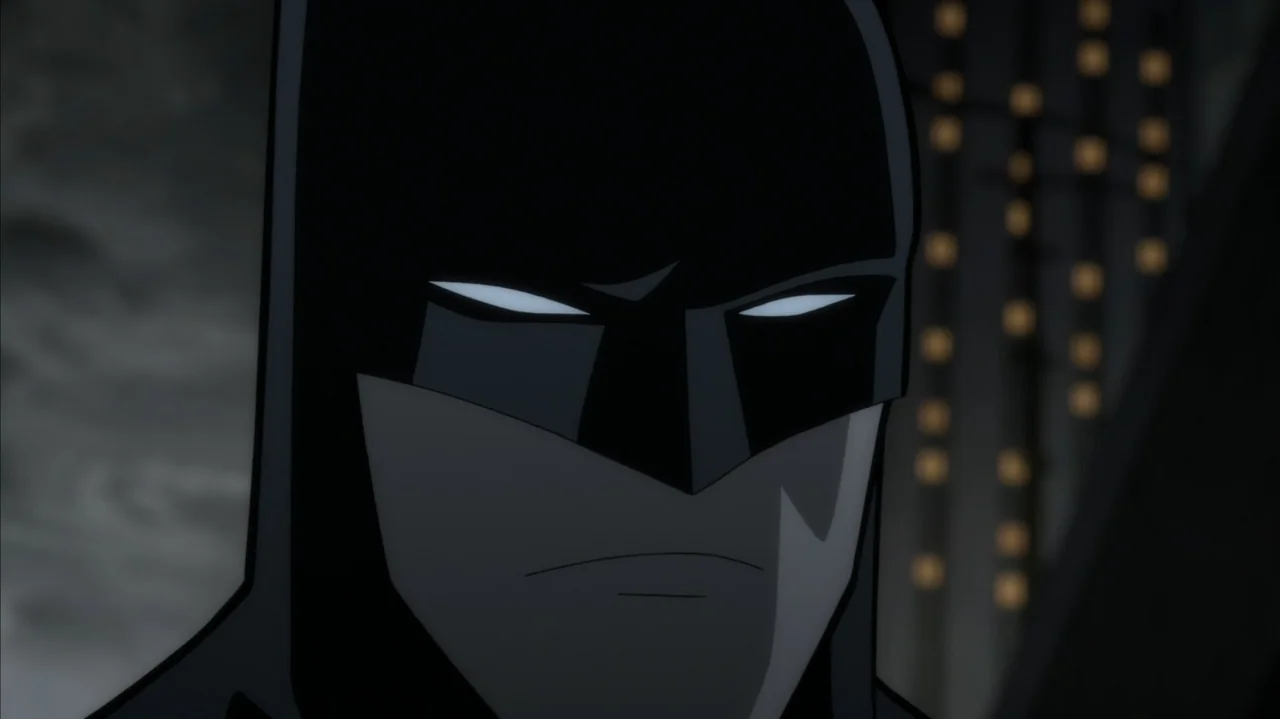 Batman: The Long Halloween, Part Two (2021) movie still: closeup — A dark night rooftop in a city with distant illuminated windows in the…