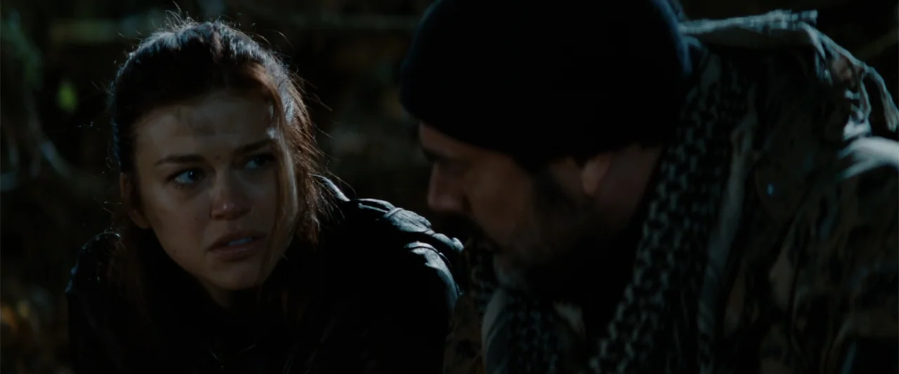 Red Dawn (2012) movie still: medium — A dark outdoor space at night with dense foliage and low lighting. A man and a woman are seated together in a…