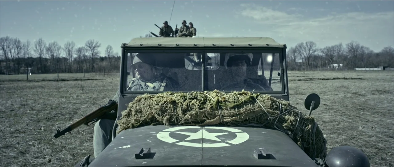 Battle of the Bulge (1965) movie still: medium — A military jeep with a white star on its hood sits in a field. Two soldiers are visible inside the…