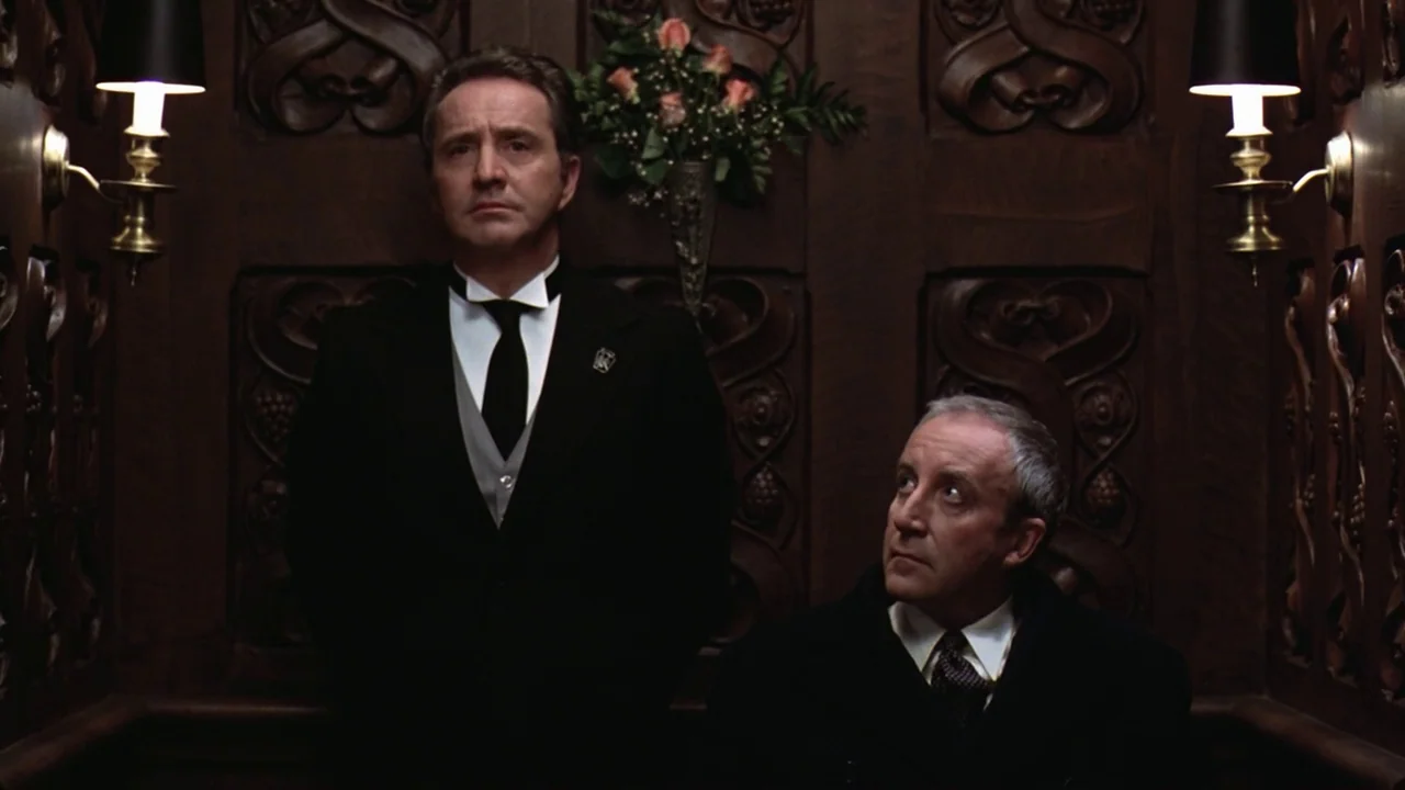 Being There (1979) movie still: medium — An elevator interior features dark, intricately carved wood paneling on the walls. Two men dressed in…