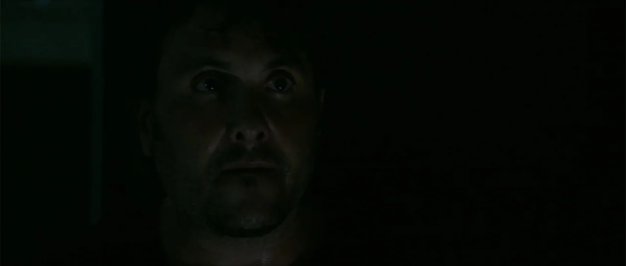 The Vault (2017) movie still: closeup — A man's face is illuminated in a dark, otherwise black interior space. The subject gazes forward with wide…